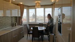 Moderní kuchyně s jídelním koutem a velkými okny, žena u stolu během dne.
